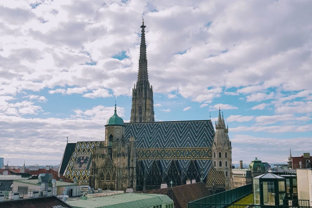 Beitragsbild: Ansicht des Wiener Stephansdom im 1. Bezirk vor blauem Himmel mit Schäfchenwolken von einer Dachterrasse aus.