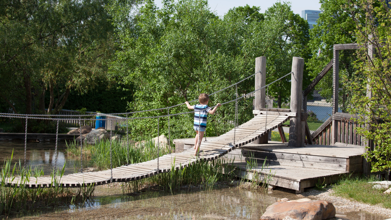 Ein Kind geht über eine Hängebrücke auf dem Wasserspielplatz auf der Donauinsel in Wien, eine sommerliche Szene