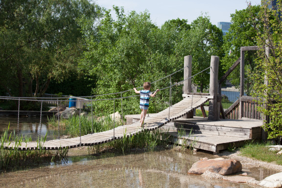 Ein Kind geht über eine Hängebrücke auf dem Wasserspielplatz auf der Donauinsel in Wien, eine sommerliche Szene