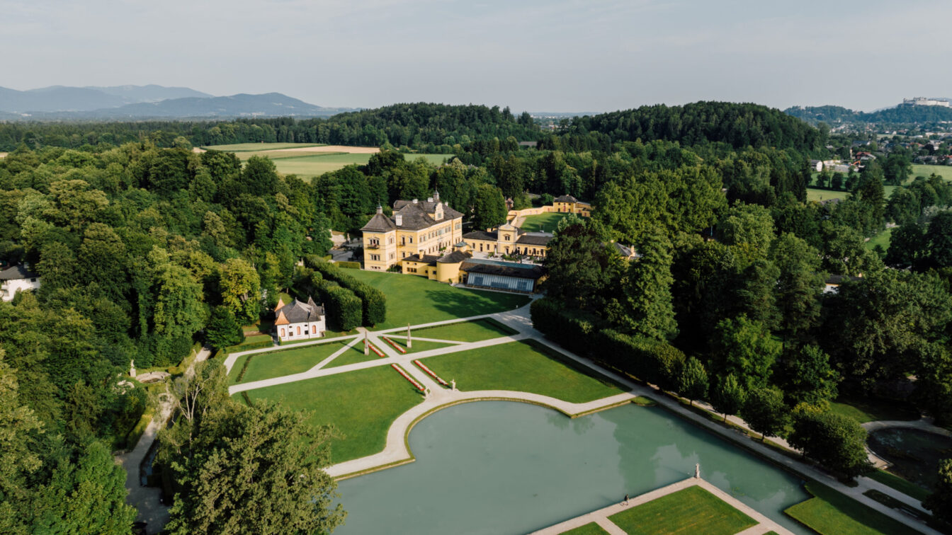 Panoramaaufnahme von Schloss Hellbrunn in Salzburg mit prächtiger Parkanlage, barockem Lustschloss und Wasserspielen, eingebettet in die grüne Naturlandschaft.