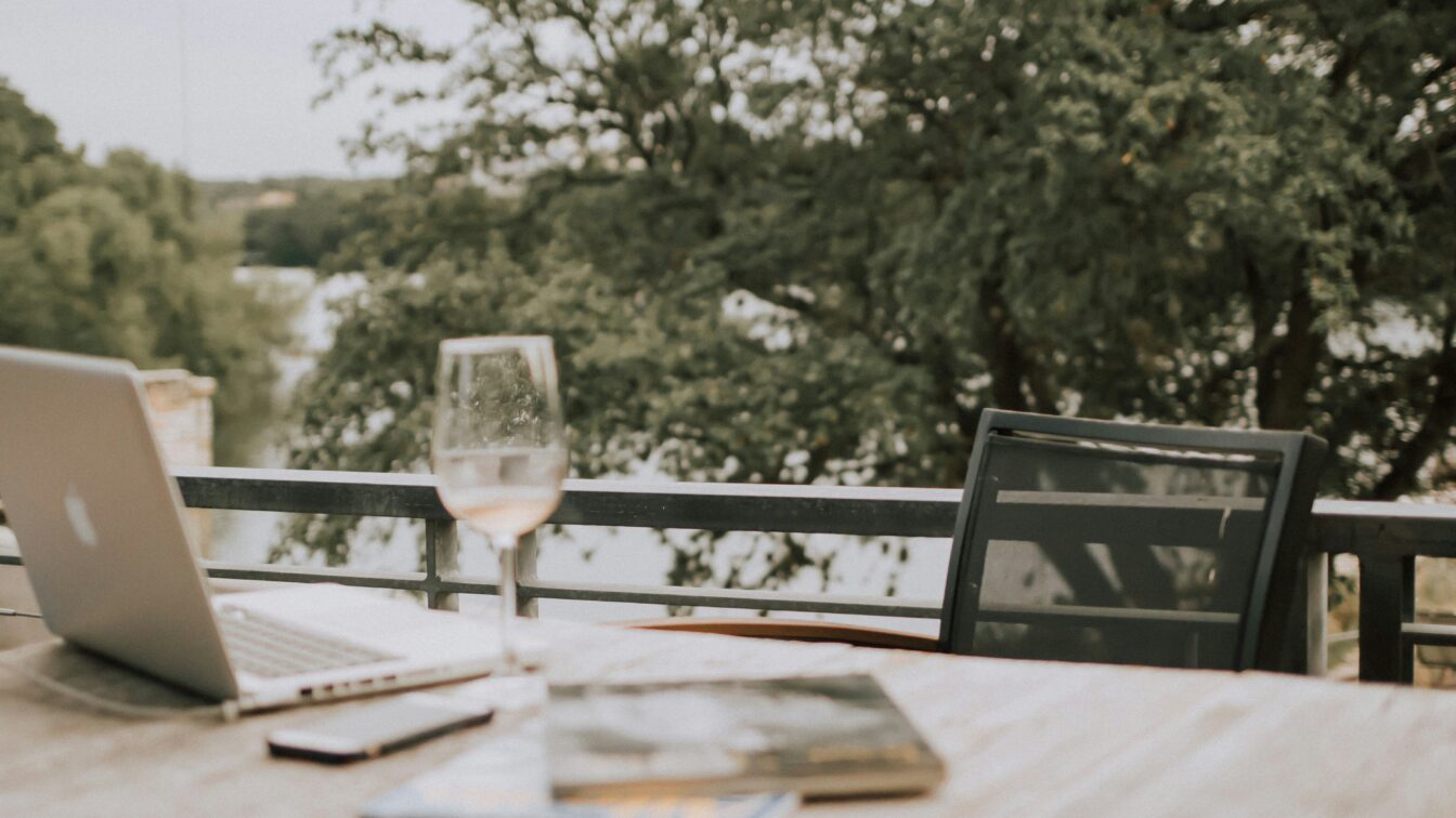 Ein Workation-Setup mit Laptop, Notizbuch und Glas in grüner Umgebung.