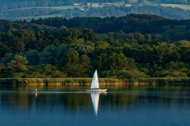 Segelboot auf dem Chiemsee bei Sonnenuntergang vor bewaldeter Hügellandschaft in Bayern