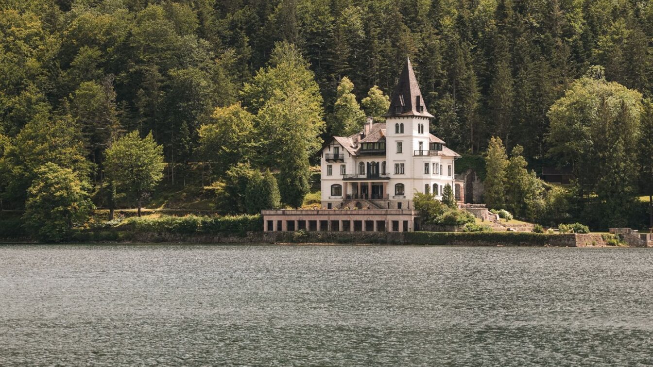 Historische Villa mit Turm direkt am Ufer des Altausseer Sees, umgeben von dichter Waldlandschaft – malerisches Anwesen im Salzkammergut, eingebettet in idyllischer Naturkulisse.