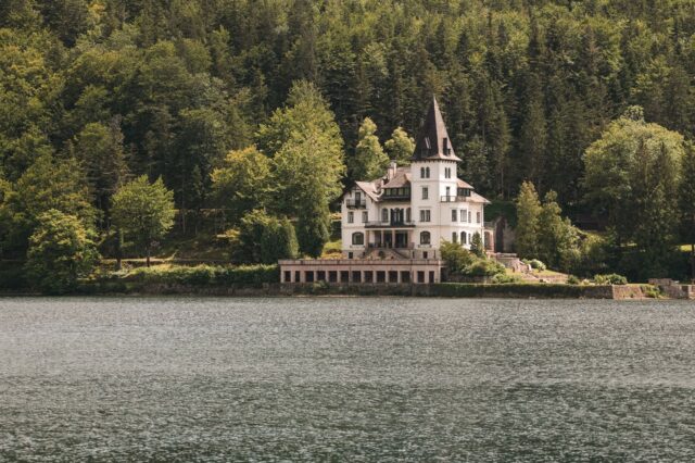 Historische Villa mit Turm direkt am Ufer des Altausseer Sees, umgeben von dichter Waldlandschaft – malerisches Anwesen im Salzkammergut, eingebettet in idyllischer Naturkulisse.