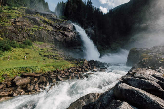 Tosende Wassermassen bei den Krimmler Wasserfällen. Zu sehen sind auch Kinder, die zum Wasserfall wandern