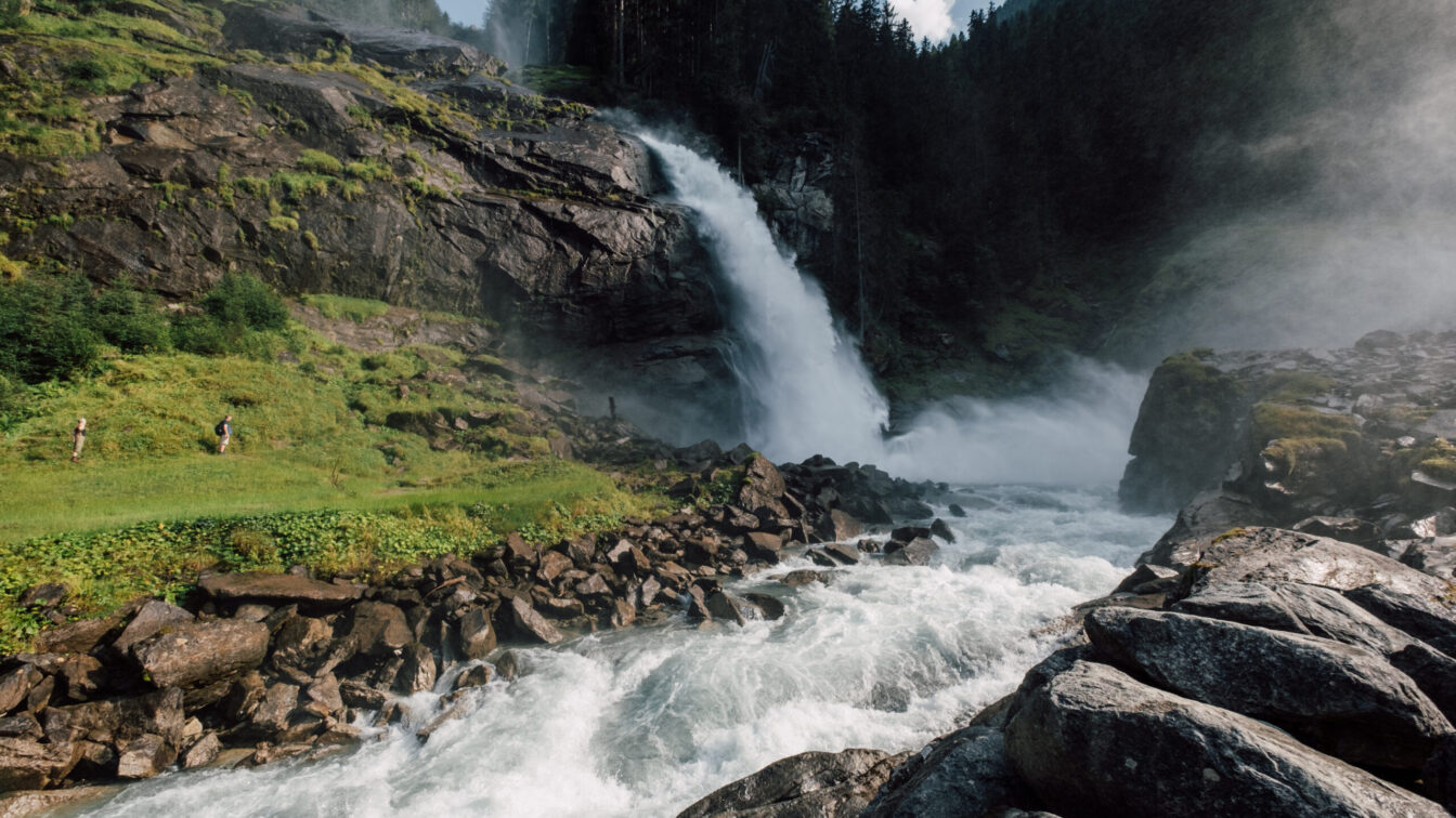 Tosende Wassermassen bei den Krimmler Wasserfällen. Zu sehen sind auch Kinder, die zum Wasserfall wandern