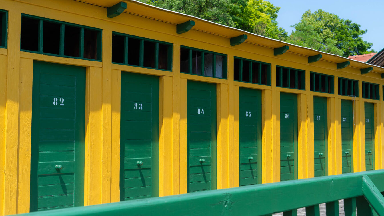 Historische Umkleidekabinen im Thermalbad Bad Fischau – bunte Holzfassade in Gelb und Grün mit nummerierten Türen, nostalgisches Flair im traditionsreichen Freibad in Niederösterreich.