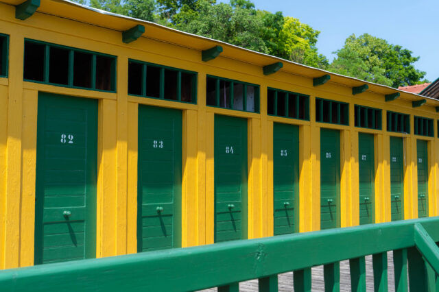 Historische Umkleidekabinen im Thermalbad Bad Fischau – bunte Holzfassade in Gelb und Grün mit nummerierten Türen, nostalgisches Flair im traditionsreichen Freibad in Niederösterreich.