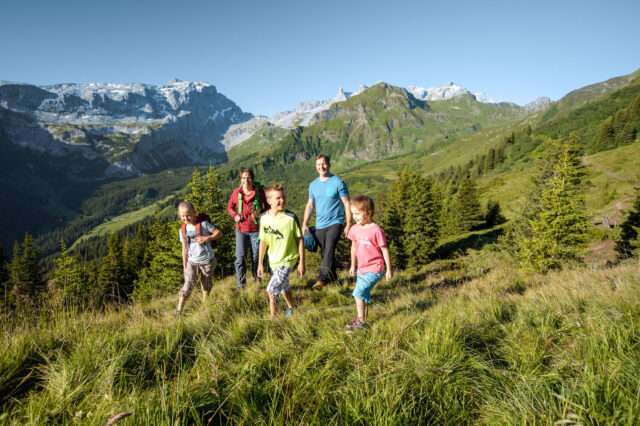 Familie beim Wandern durch grüne Wiesen bei Sonnenschein am Golm Erlebnisberg in Vorarlberg
