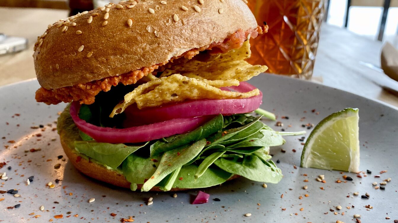 Veganer Burger mit Nachos und Babyspinat auf einem Teller