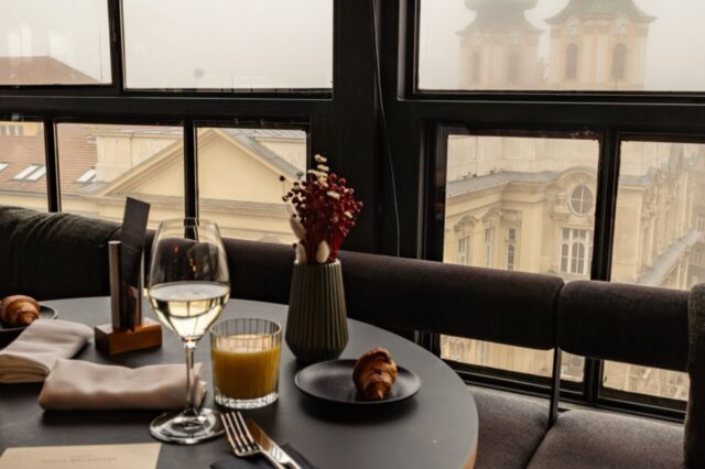 Stilvoll gedeckter Frühstückstisch in einem der besten Hotels Budapests mit Blick auf historische Fassaden und nebelverhangene Kirchtürme – elegantes Ambiente über den Dächern der Stadt