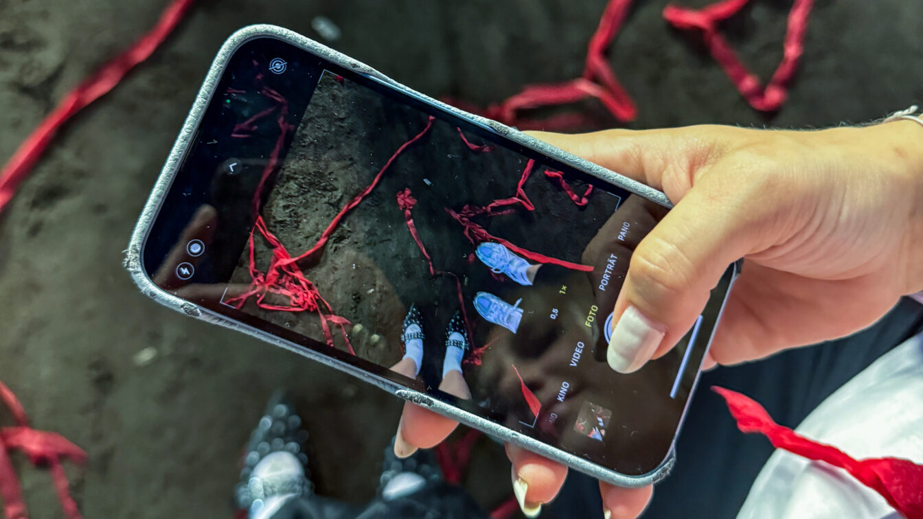 Nahaufnahme einer Hand mit Smartphone, das ein kreatives Foto von zwei Personen auf einem mit roten Bändern bedeckten Tanzboden zeigt – festgehaltene Momentaufnahme in einem Berliner Club. Die Szene deutet auf ein lebendiges Nachtleben und künstlerisch inszenierte Clubkultur in Berlin hin.