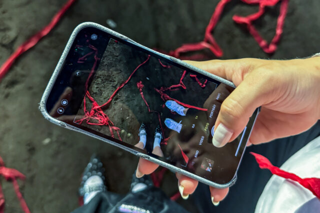 Nahaufnahme einer Hand mit Smartphone, das ein kreatives Foto von zwei Personen auf einem mit roten Bändern bedeckten Tanzboden zeigt – festgehaltene Momentaufnahme in einem Berliner Club. Die Szene deutet auf ein lebendiges Nachtleben und künstlerisch inszenierte Clubkultur in Berlin hin.