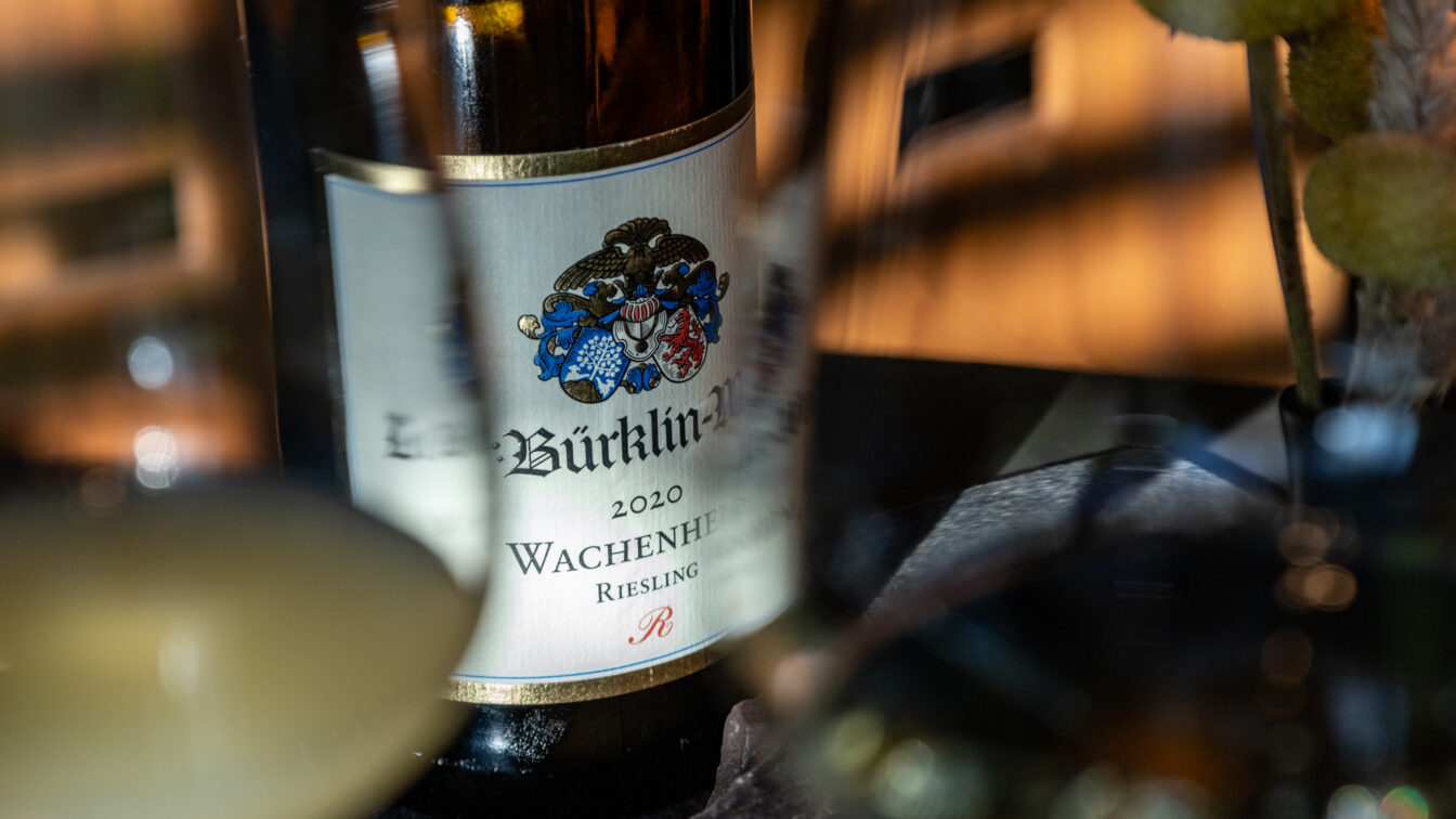 Nahaufnahme einer edlen Weinflasche vom Weingut Bürklin-Wolf, Jahrgang 2020, Wachenheimer Riesling, in stilvoller Atmosphäre mit gedämpftem Licht und eleganten Gläsern – typische Szene in einer gehobenen Weinbar in Berlin, ideal für Genießer und Weinliebhaber.