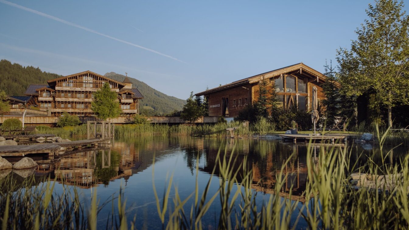 Exklusive Chalets in den Bergen – das Naturresort Puradies in Leogang mit Holzchalets am Badeteich und Alpenblick im Sommer