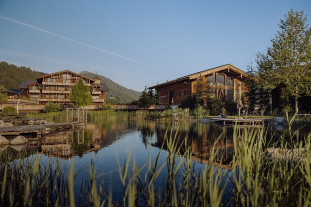 Exklusive Chalets in den Bergen – das Naturresort Puradies in Leogang mit Holzchalets am Badeteich und Alpenblick im Sommer