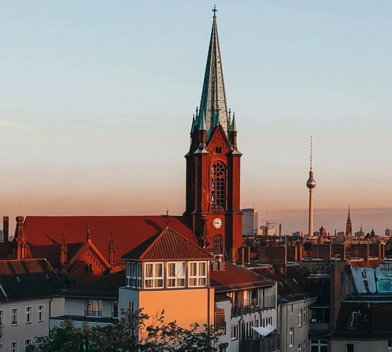 Blick auf die Gethsemanekirche im Berliner Stadtteil Prenzlauer Berg bei Sonnenuntergang mit dem Berliner Fernsehturm im Hintergrund – architektonisches Highlight im Prenzlauer Berg Guide und beliebter Fotospot in Berlin.
