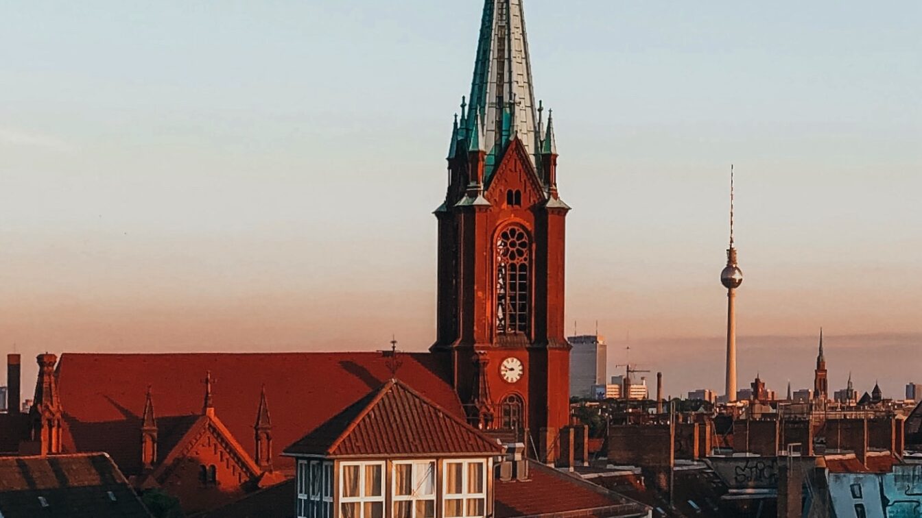 Blick auf die Gethsemanekirche im Berliner Stadtteil Prenzlauer Berg bei Sonnenuntergang mit dem Berliner Fernsehturm im Hintergrund – architektonisches Highlight im Prenzlauer Berg Guide und beliebter Fotospot in Berlin.