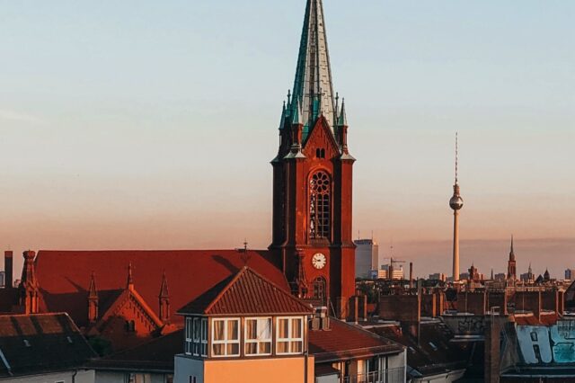 Blick auf die Gethsemanekirche im Berliner Stadtteil Prenzlauer Berg bei Sonnenuntergang mit dem Berliner Fernsehturm im Hintergrund – architektonisches Highlight im Prenzlauer Berg Guide und beliebter Fotospot in Berlin.