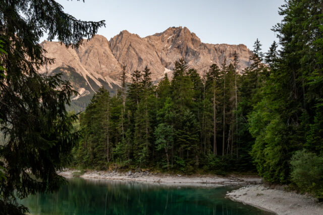 Blick auf die Zugspitze bei Sonnenuntergang vom Eibsee bei Garmisch-Partenkirchen in Bayern – klare Berglandschaft mit grünem Wald und türkisfarbenem Wasser im Vordergrund.