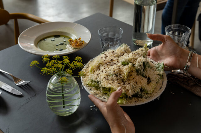 Detailaufnahme eines kunstvoll angerichteten Essens in einem außergewöhnlichen Restaurant in Berlin: Ein großer Caesar Salad mit reichlich frisch geriebenem Käse und eine grüne Suppe mit Öl-Perlen, serviert in modernem Ambiente mit stilvoller Tischdekoration – ein kulinarisches Erlebnis für Feinschmecker.