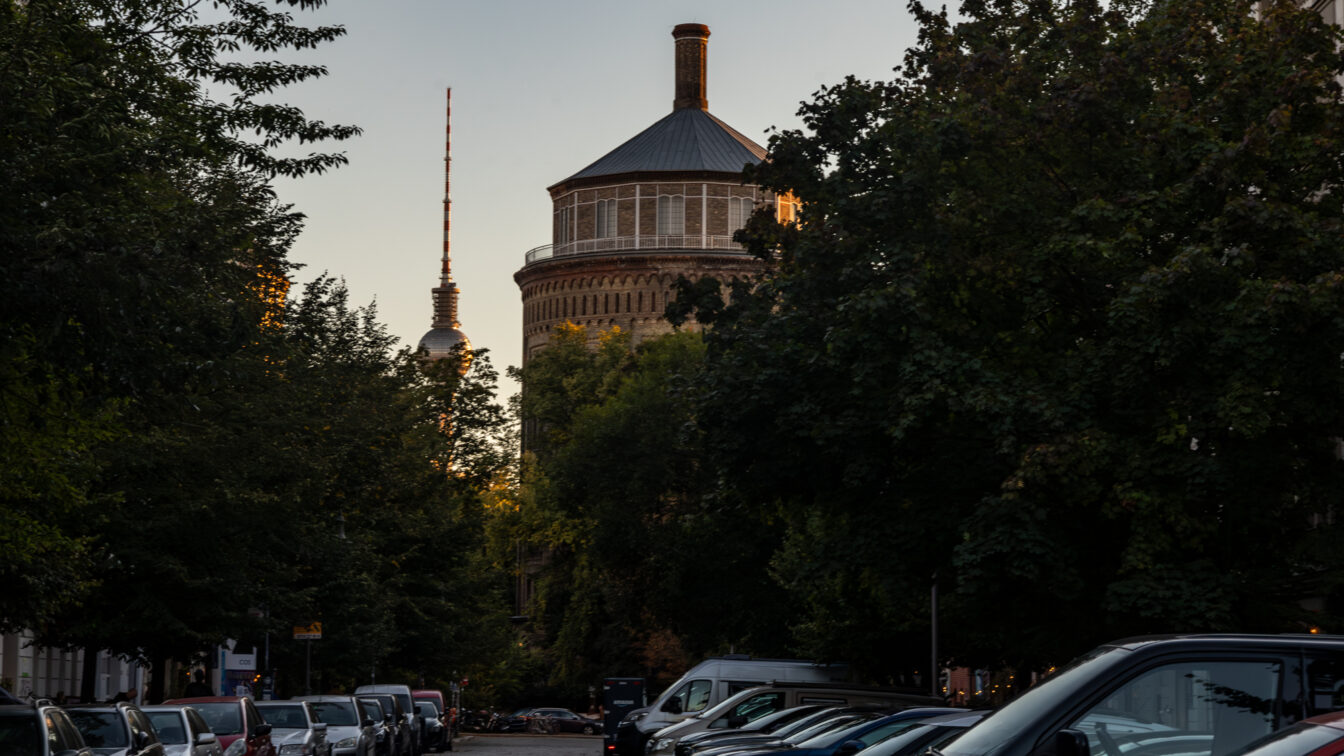 Baumbestandene Berliner Straße mit parkenden Autos in der Rykestraße in Prenzlauer Berg, im Hintergrund der Wasserturm und der Fernsehturm im Abendlicht.