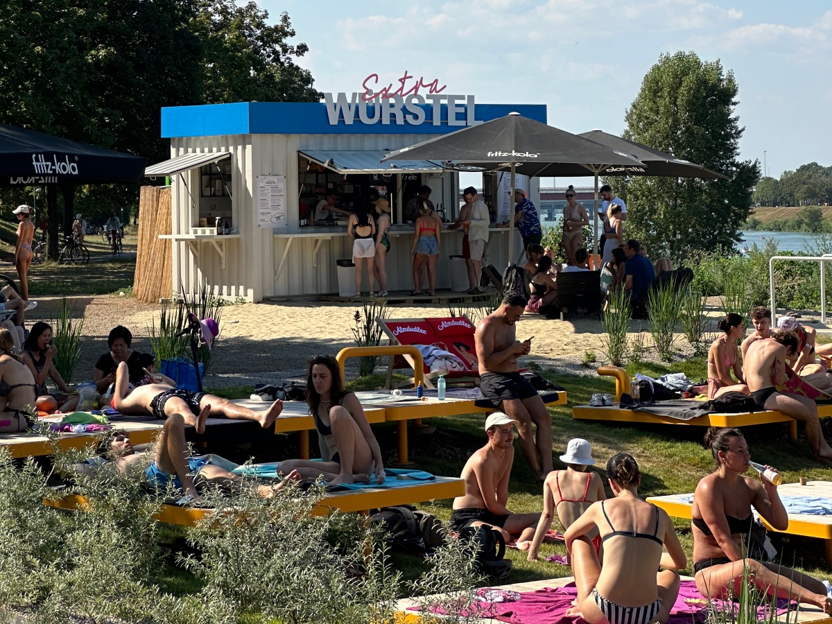 Menschen sonnen sich auf der Donauinsel vor dem Würstelstand Extra Würstel