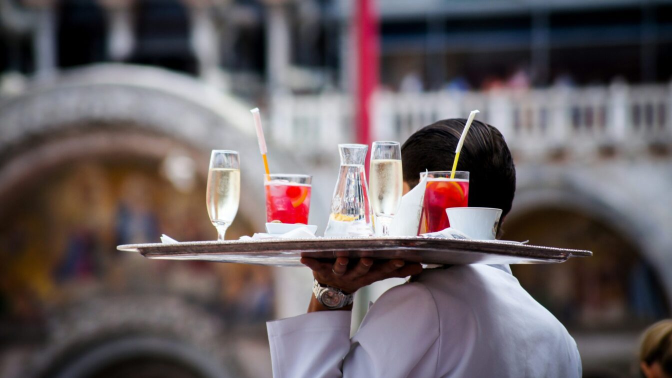 ein Kellner trägt ein mit Drinks beladenes Tablett