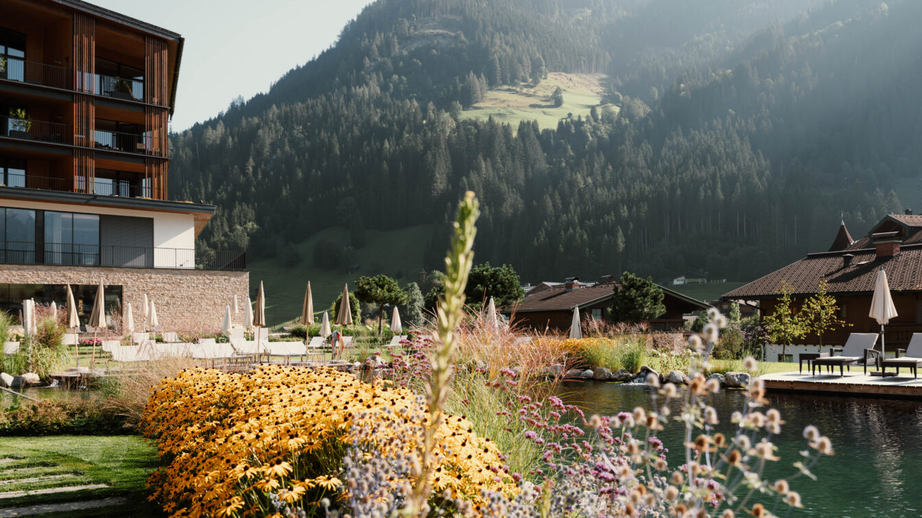 Familienfreundliches Hotel in den österreichischen Alpen mit Naturpool, gemütlicher Sonnenterrasse und blühendem Sommergarten – ideal für einen entspannten Familienurlaub in der Natur