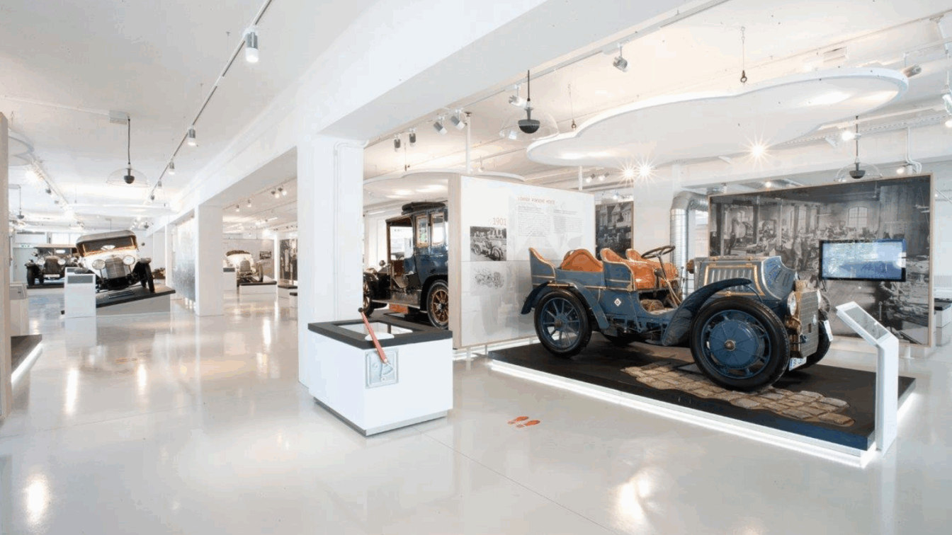 Innenansicht des fahr(T)raum Museums mit historischen Automobilen, darunter der Lohner-Porsche Mixte von 1901, ausgestellt in moderner, heller Umgebung – ideal für Technik- und Autogeschichte-Enthusiasten.