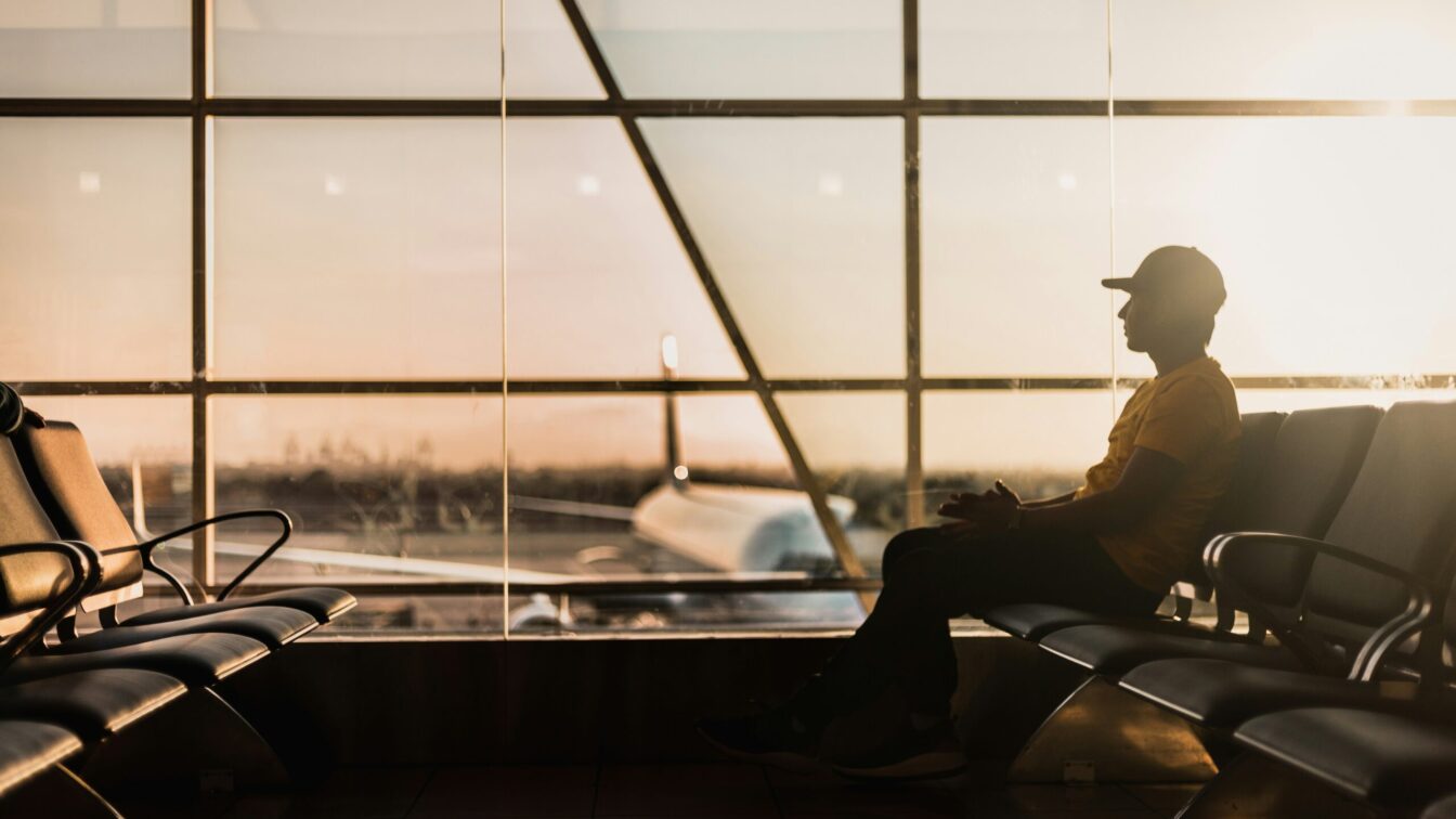 Mann sitzt bei Sonnenaufgang im Wartebereich eines Flughafens, Blick auf ein Flugzeug am Gate – ruhige Reisestimmung vor dem Abflug, modernes Terminal im Gegenlicht.
