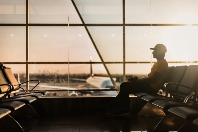 Mann sitzt bei Sonnenaufgang im Wartebereich eines Flughafens, Blick auf ein Flugzeug am Gate – ruhige Reisestimmung vor dem Abflug, modernes Terminal im Gegenlicht.