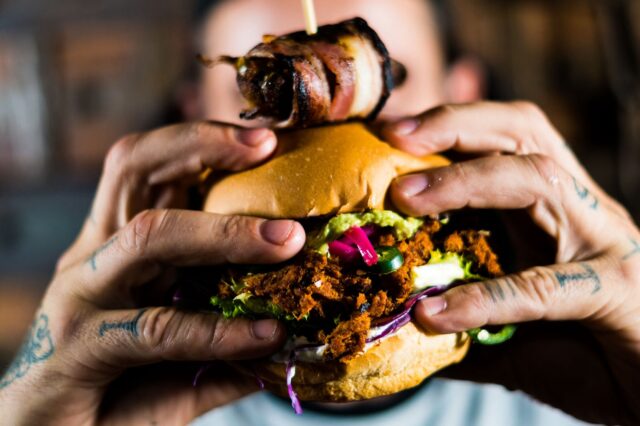 Ein Mann hält einen Burger in die Kamera