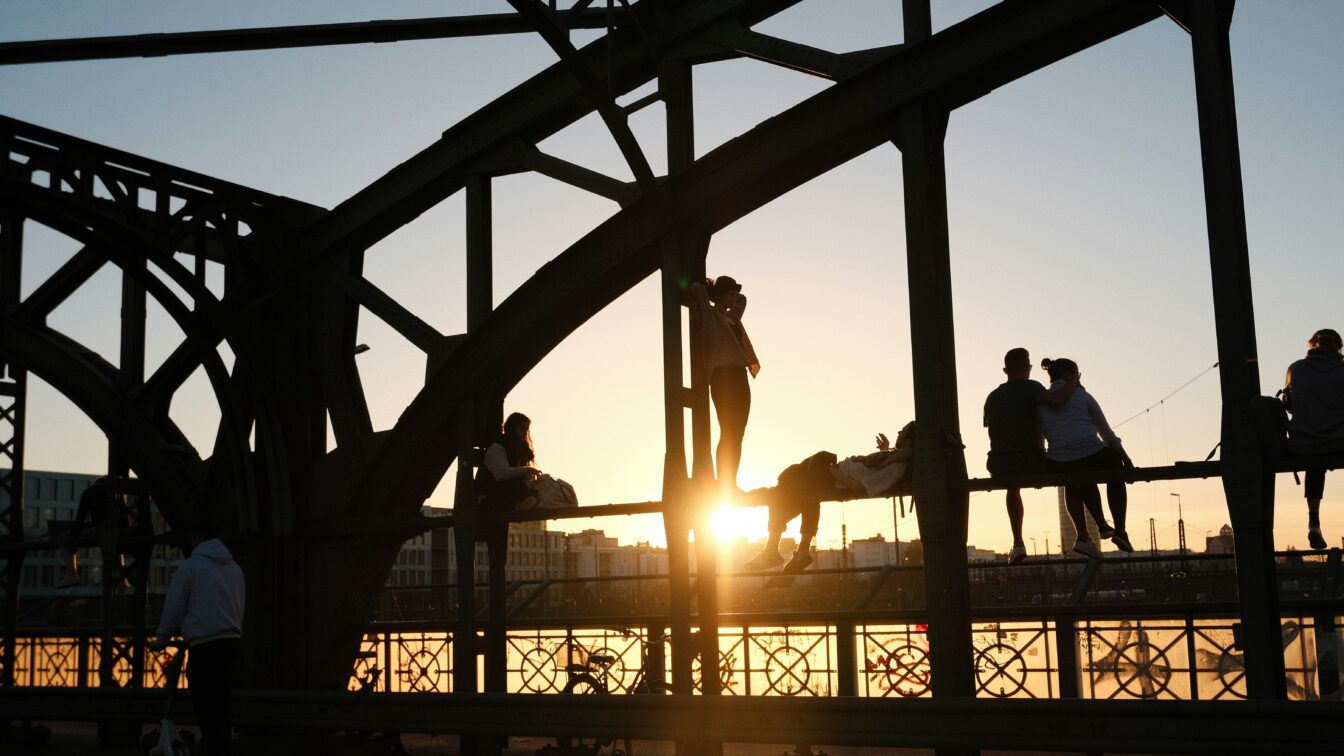 Eine Gruppe von Menschen, die bei Sonnenuntergang auf einer Brücke, der Hackerbrücke in München, stehen