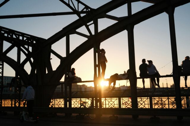 Eine Gruppe von Menschen, die bei Sonnenuntergang auf einer Brücke, der Hackerbrücke in München, stehen