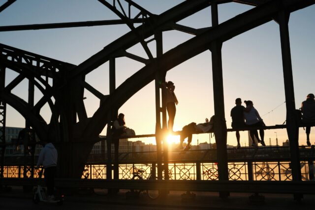 Eine Gruppe von Menschen, die bei Sonnenuntergang auf einer Brücke, der Hackerbrücke in München, stehen