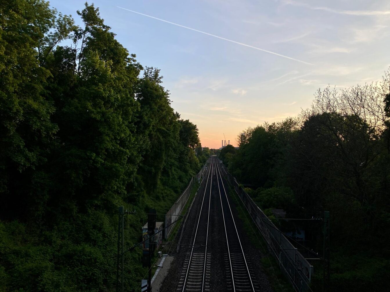 Blick über ein Gleisbett und ins Grüne vom Schmederersteg bei Sonnenuntergang in München.