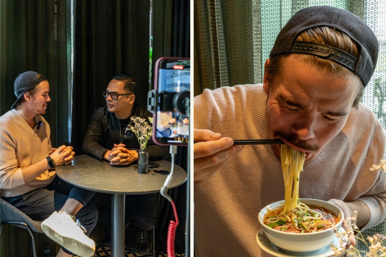 Zwei Personen im Gespräch bei einem Interview im Vina Graz, daneben ein Gast, der genüsslich eine Schüssel dampfender Nudelsuppe mit Stäbchen isst.