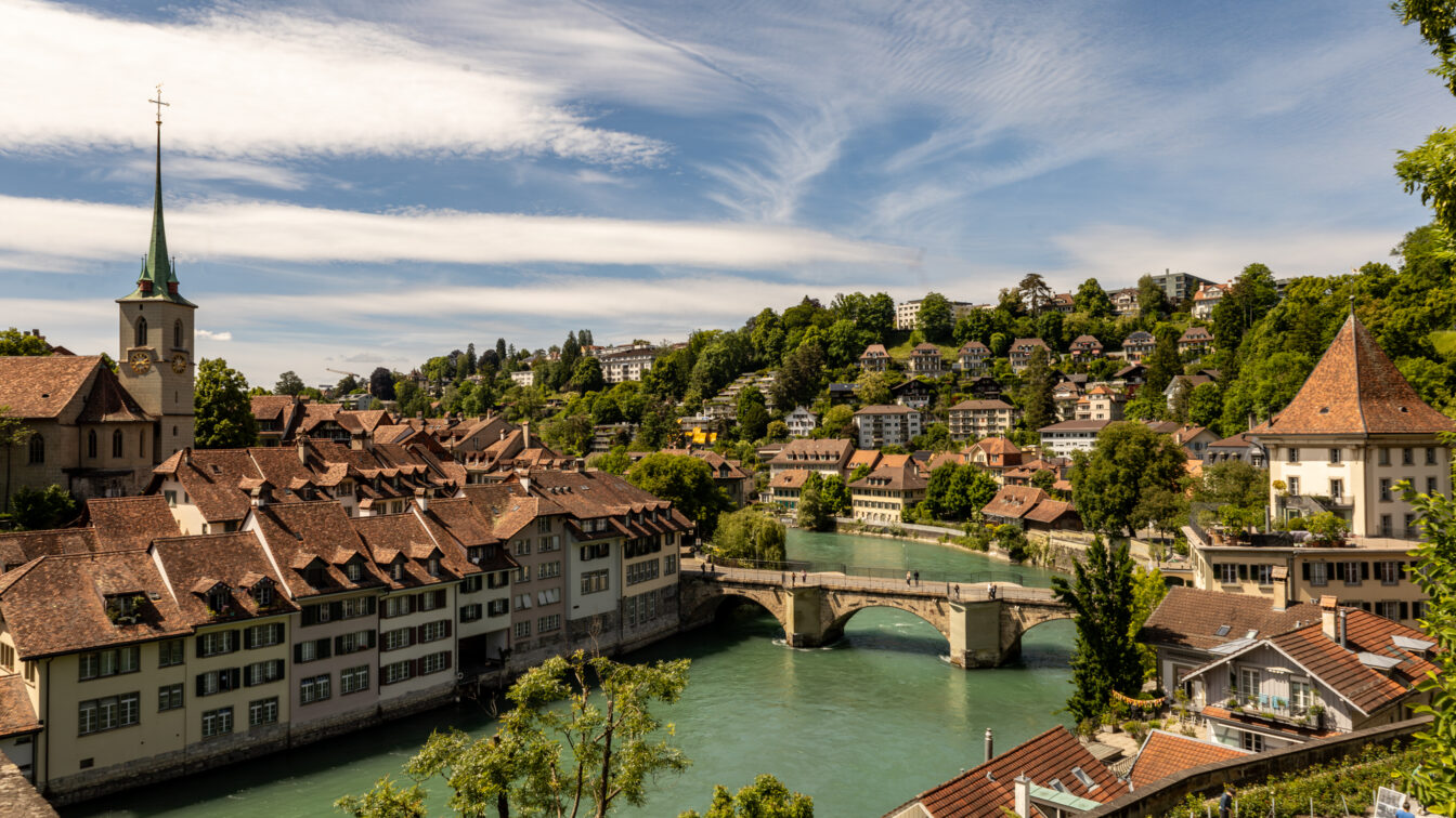 Panoramablick auf die Altstadt von Bern in der Schweiz mit der Aare, historischen Häusern mit roten Dächern, der Nydeggbrücke und der Kirche Nydeggkirche – beliebtes Fotomotiv und Ausflugsziel in der UNESCO-Weltkulturerbe-Stadt Bern.
