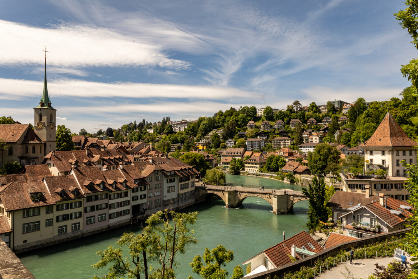 Panoramablick auf die Altstadt von Bern in der Schweiz mit der Aare, historischen Häusern mit roten Dächern, der Nydeggbrücke und der Kirche Nydeggkirche – beliebtes Fotomotiv und Ausflugsziel in der UNESCO-Weltkulturerbe-Stadt Bern.
