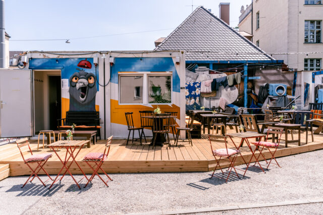 Eine hözerne Terrasse vor einem Café, das mit Graffiti-Kunst verziert ist.