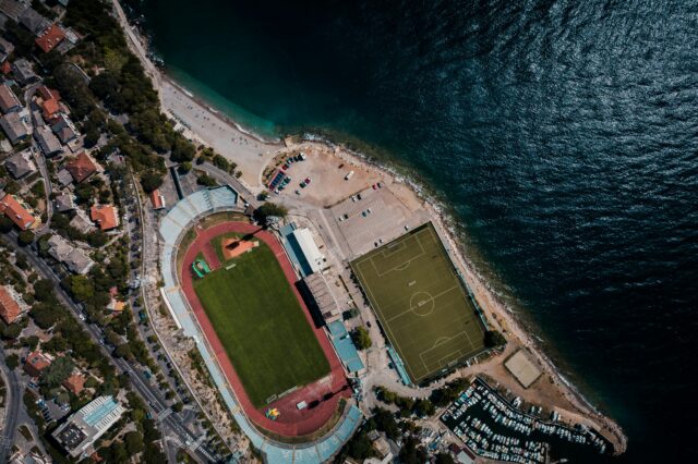 Eine Stadt am Meer mit Fußballstadion und Sportplatz aus der Vogelperspektive.
