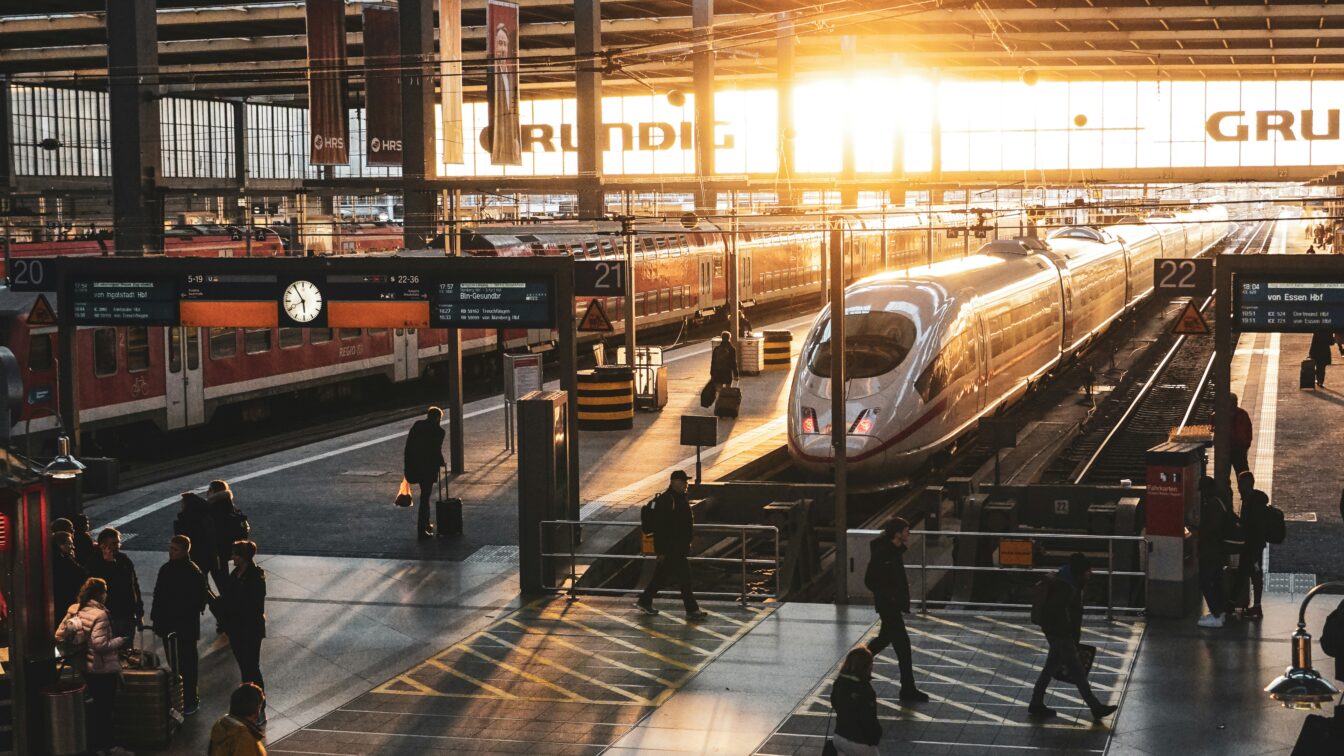 ICE-Zug am Bahnsteig im Hauptbahnhof bei Sonnenaufgang – Reisende auf dem Weg zum Gleis, moderne Bahnreise in Deutschland mit Lichtstimmung im Morgenverkehr.