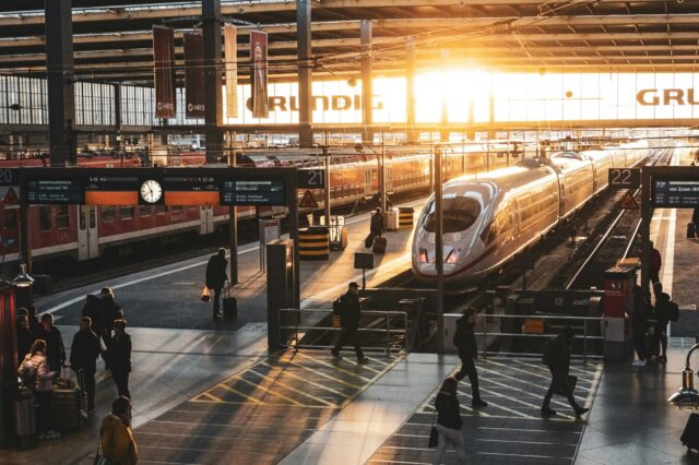 ICE-Zug am Bahnsteig im Hauptbahnhof bei Sonnenaufgang – Reisende auf dem Weg zum Gleis, moderne Bahnreise in Deutschland mit Lichtstimmung im Morgenverkehr.