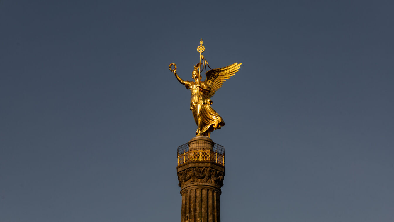 Goldene Statue der Viktoria auf der Berliner Siegessäule vor klarem, blauem Himmel im Abendlicht