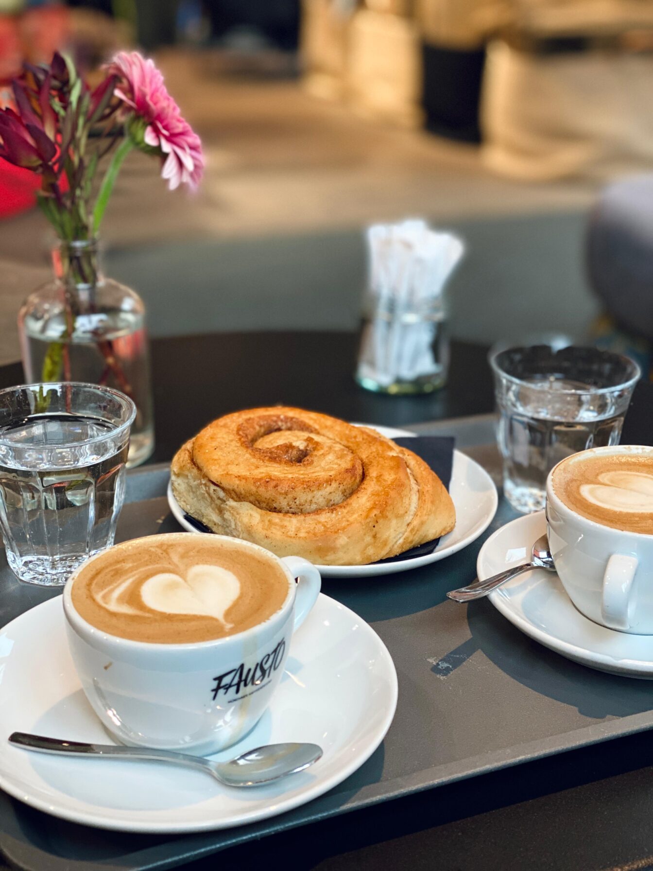 Ein dunkler Tisch gedeckt mit rosa Blumen, Kaffee und Zimtschnecke.