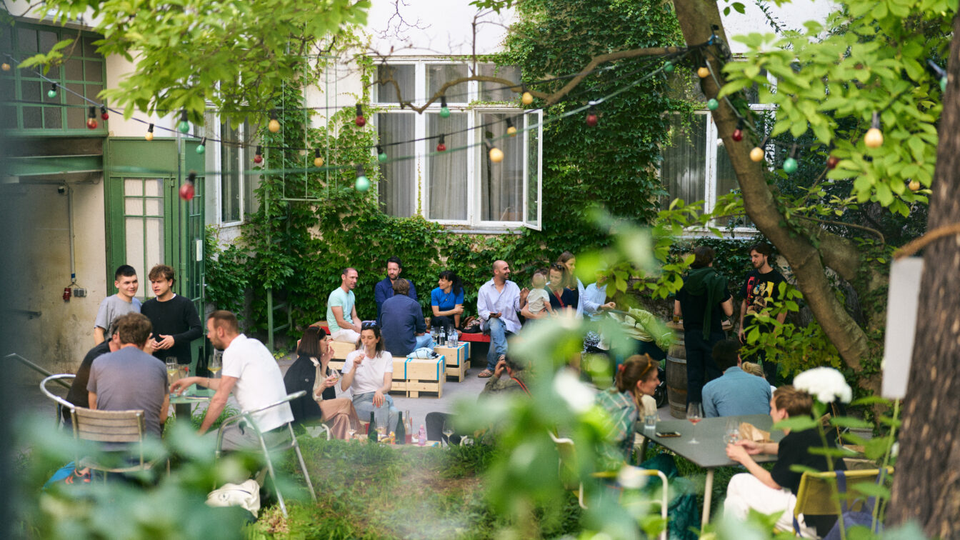 Menschen in einem grünen Innenhof, die trinken und essen.
