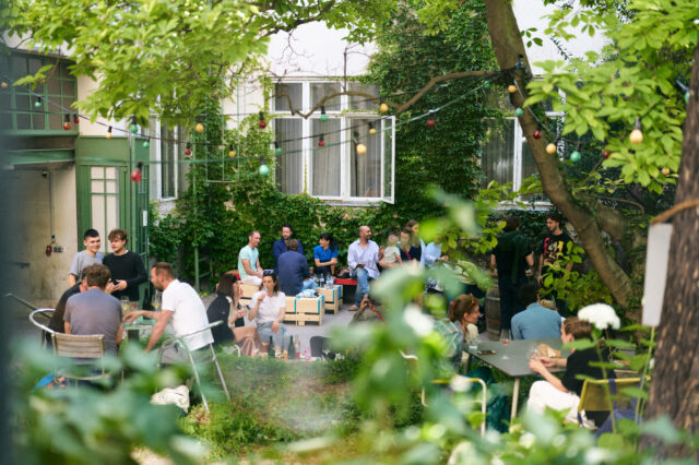 Menschen in einem grünen Innenhof, die trinken und essen.