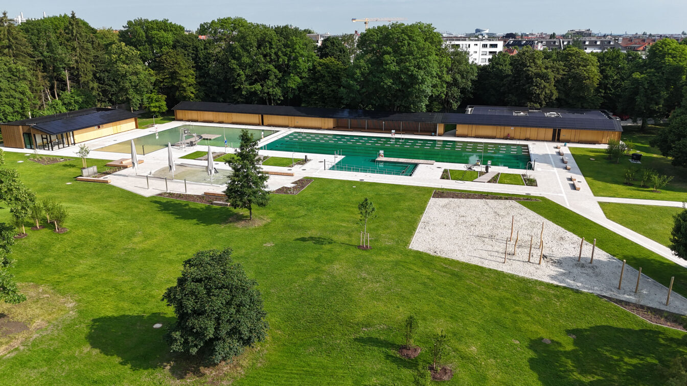 Weitläufige Grünfläche und ein naturbelassener Pool in einem Freibad in München.