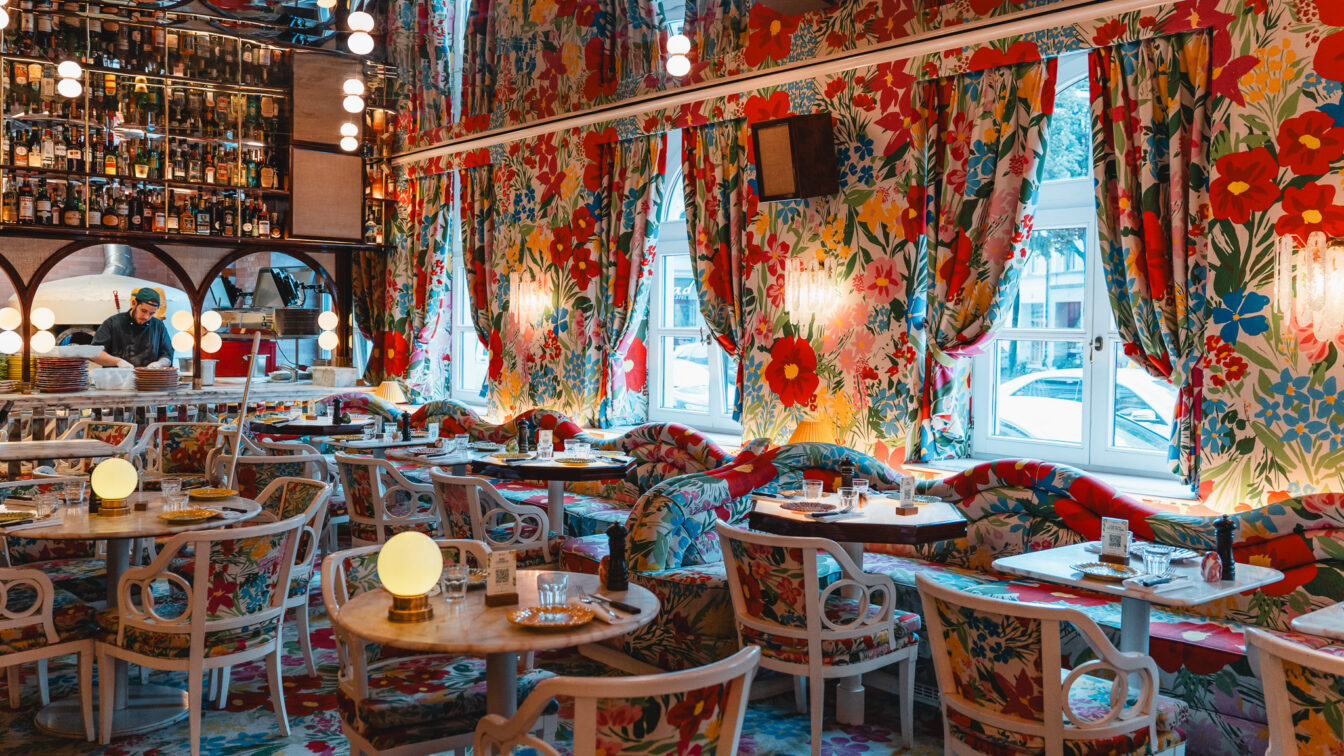 Ein bunter Innenraum eines Restaurants in München mit Blumentapete und kitschigen Details.